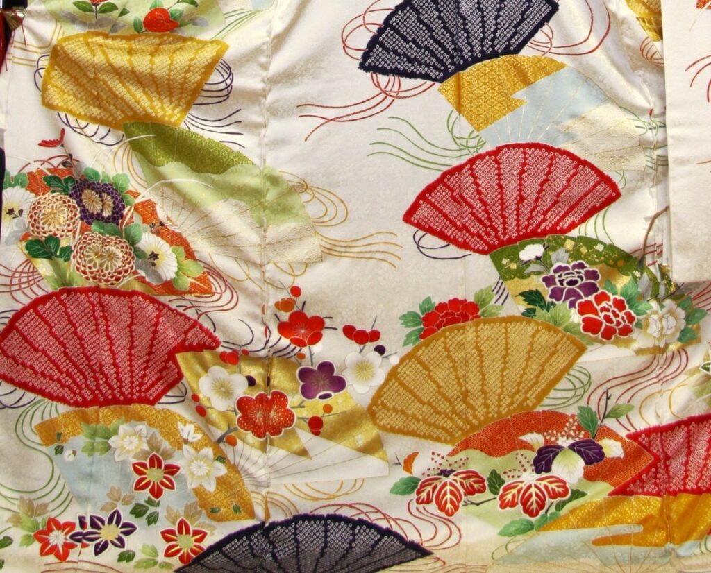 白地に色とりどりの扇面と菊・梅・牡丹が舞う振袖の柄アップ