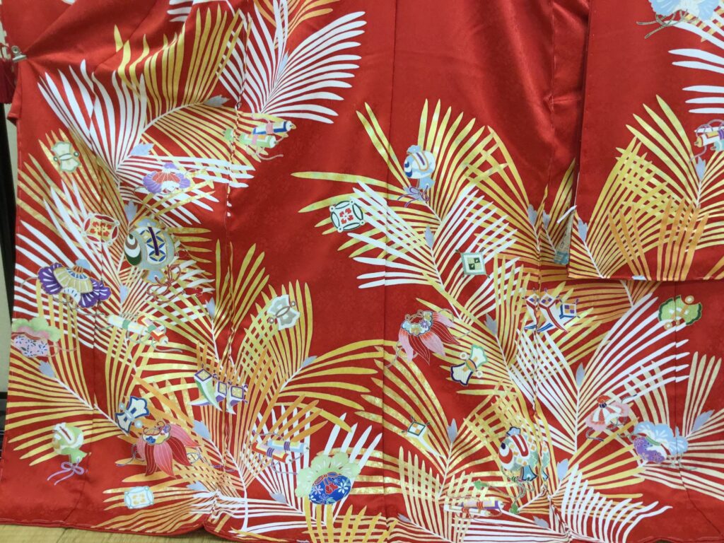 朱赤地に棕櫚の葉と手毬・独楽・花籠の御所遊び文様を配した華やかな振袖の生地アップ|染と呉服はっとり